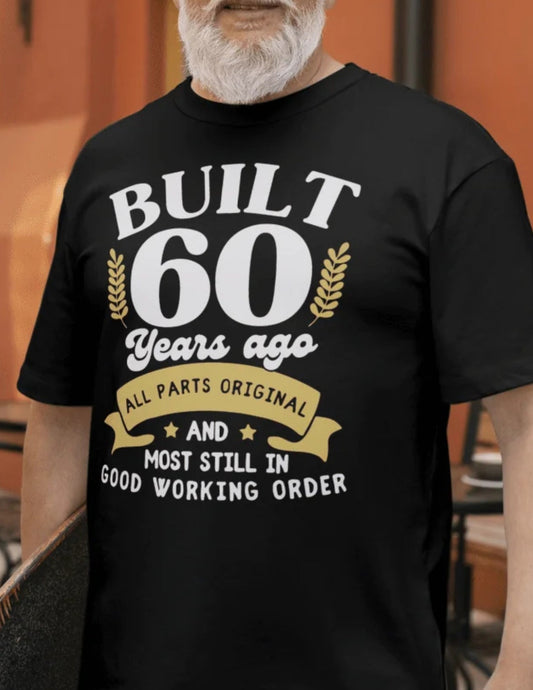 Older man wearing a black T-shirt that says “Built 60 Years Ago – All Parts Original and Most Still in Good Working Order”.