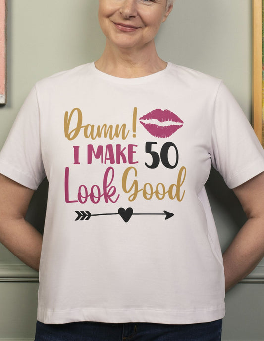 Woman wearing a white t-shirt that says “Damn! I Make 50 Look Good” with kiss mark and arrow design.