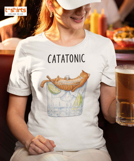 Person wearing a white t-shirt with 'CATATONIC' design and holding a drink.