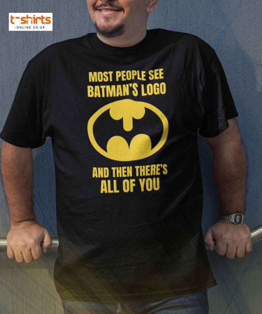 Person wearing a black t-shirt with yellow Batman logo and text against a blue wall.
