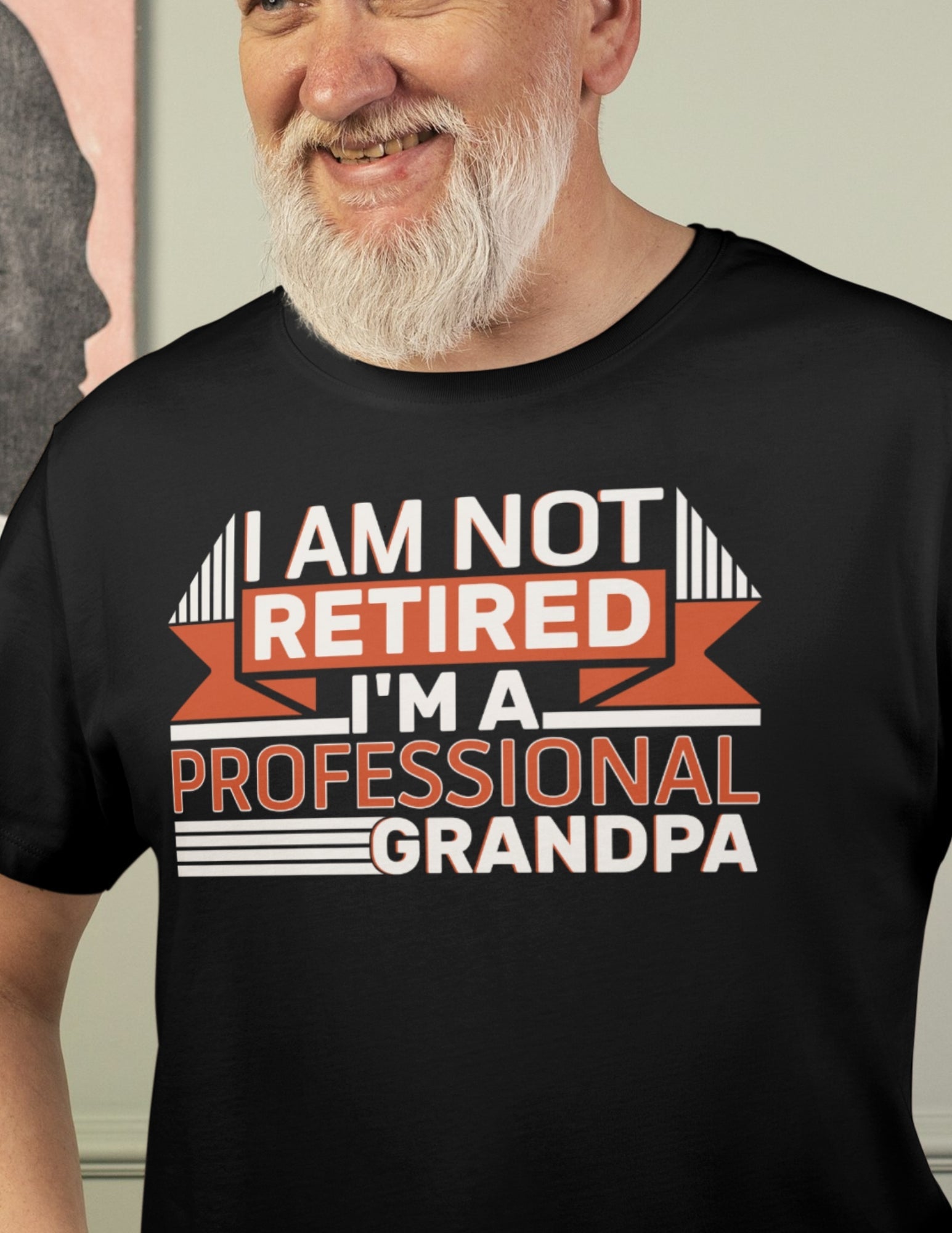 Smiling man wearing a black t-shirt that reads “I’m Not Retired, I’m a Professional Grandpa” in orange and white lettering.