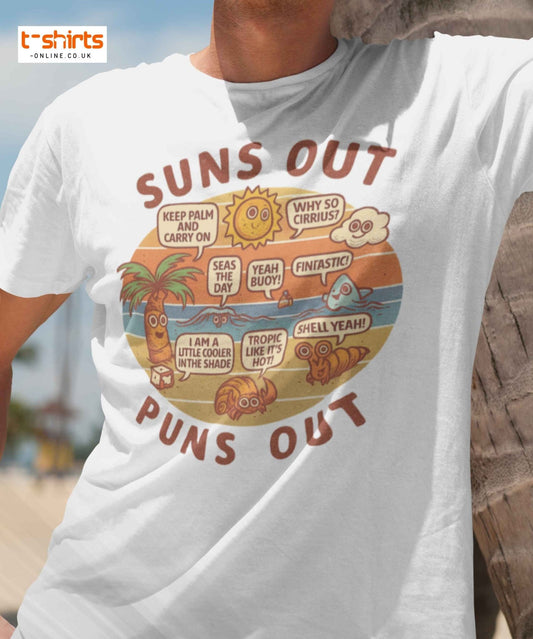 White t-shirt with a colorful graphic and text 'Suns Out Puns Out' worn by a person at a beach.