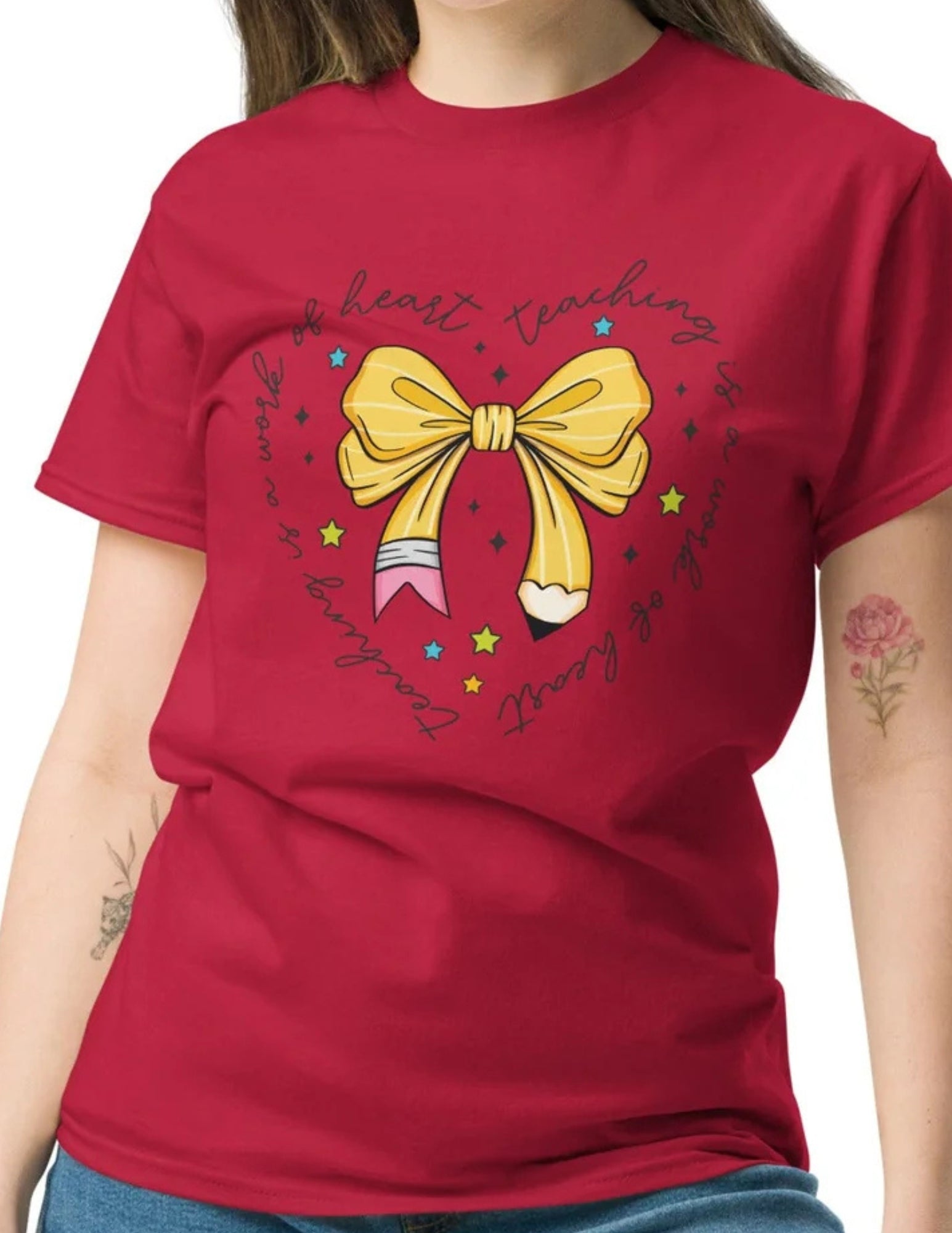 Cardinal red teacher t-shirt with yellow pencil bow and the phrase “Teaching Is a Work of Heart” in script.