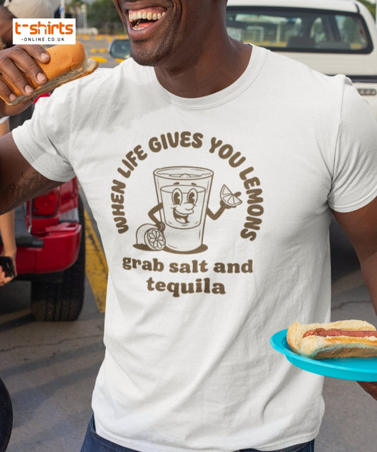 Person wearing a t-shirt with a humorous graphic and text, holding a hot dog.