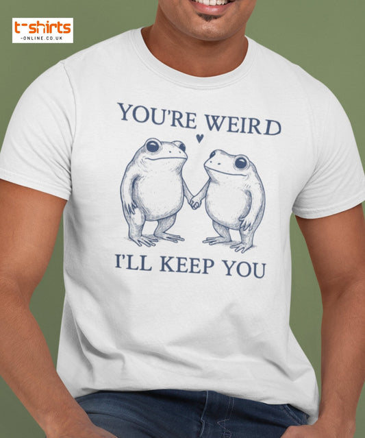 Person wearing a white t-shirt with frog graphic and text 'You're Weird, I'll Keep You' on a green background.